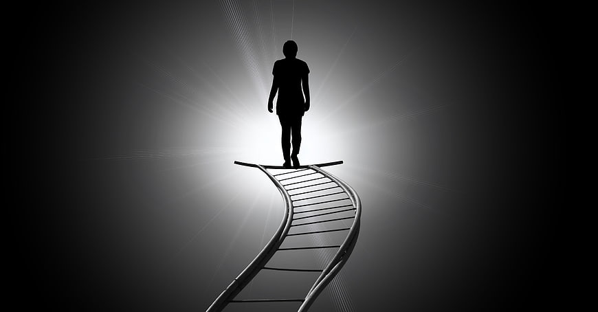 Silhouette of person standing on DNA helix ladder reaching for light