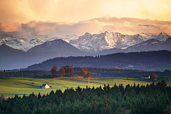 Alpine Mountain Landscape With Snowy Peaks And Green Pastures At Sunset