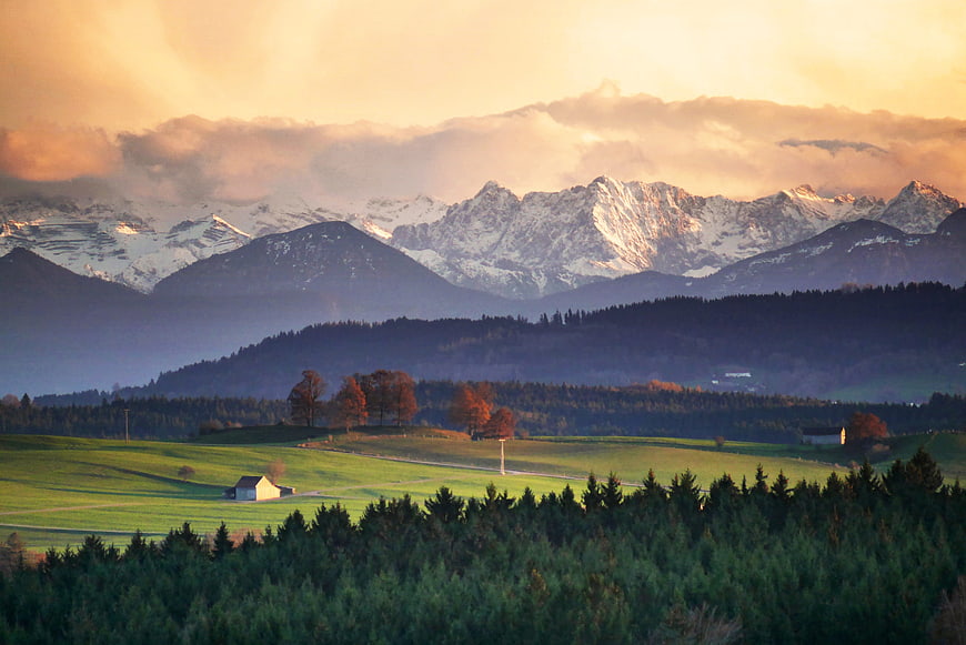 Alpine Mountain Landscape With Snowy Peaks And Green Pastures At Sunset