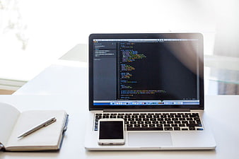 Laptop with code, smartphone, and notebook on white desk