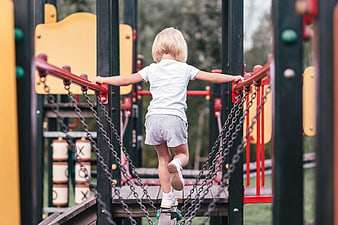 Toddler girl climbing on playground bridge