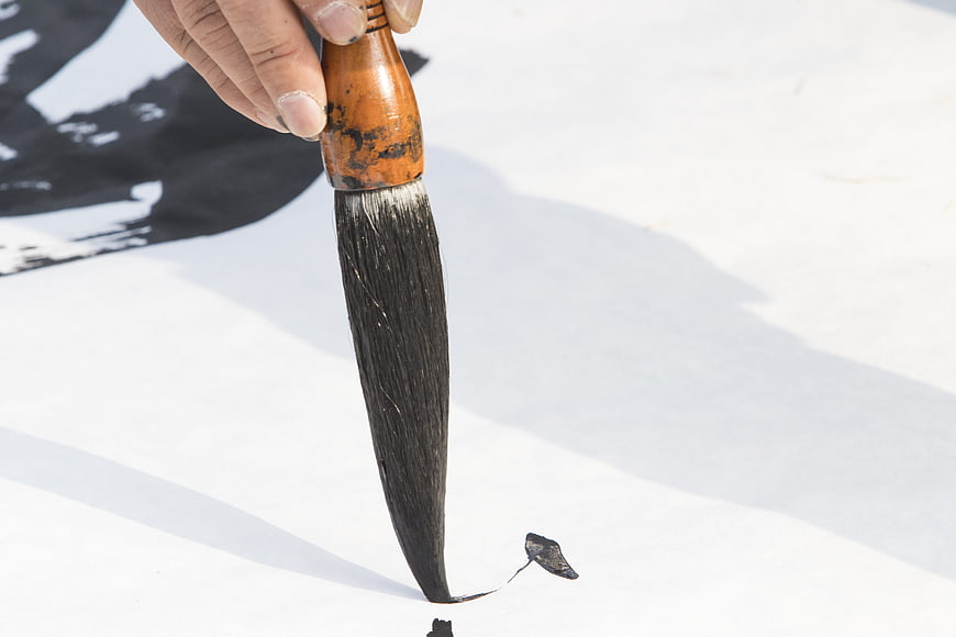 Close-up of hand holding traditional calligraphy brush with black ink