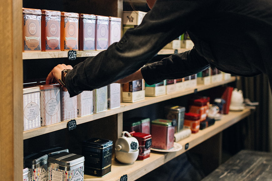 Person selecting tea tin from wooden shelf in specialty shop