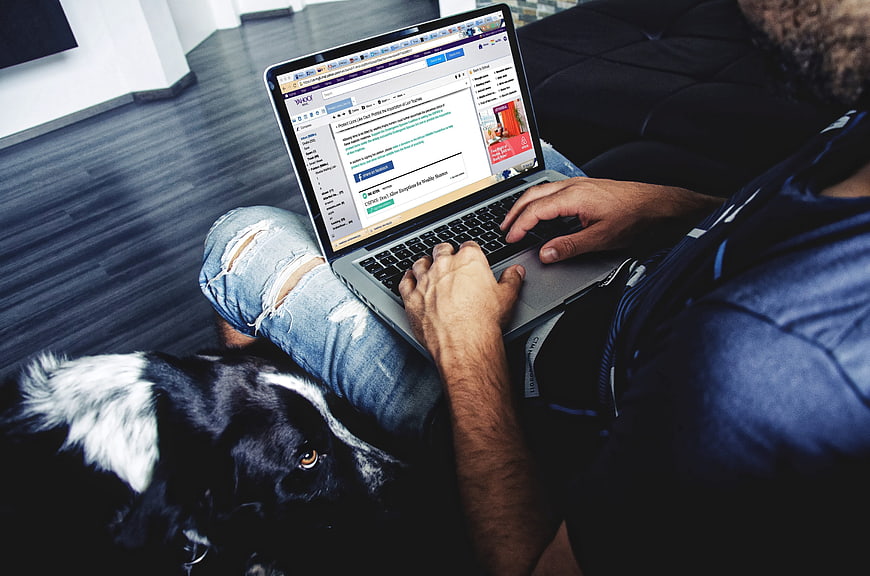 Man working on laptop with dog on couch