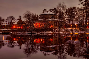 Snowy historic buildings with warm lights reflecting in calm water