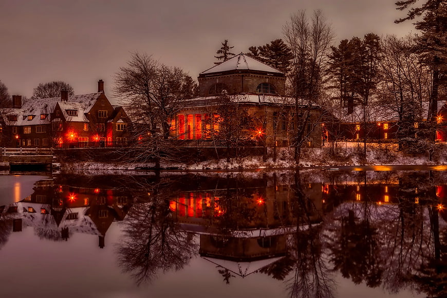 Snowy historic buildings with warm lights reflecting in calm water