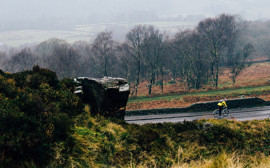 Cyclist riding on rural road through misty highland landscape