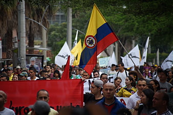 Crowd Marching With Colombian Flag And Red Banner In City Street