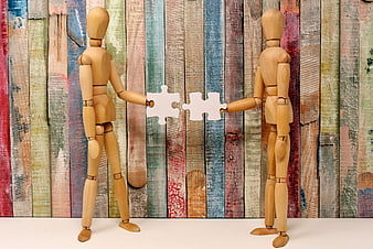 Wooden mannequins connecting puzzle pieces on colorful background