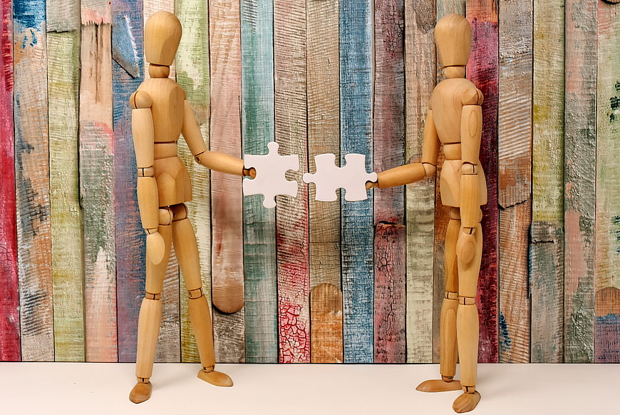 Wooden mannequins connecting puzzle pieces on colorful background