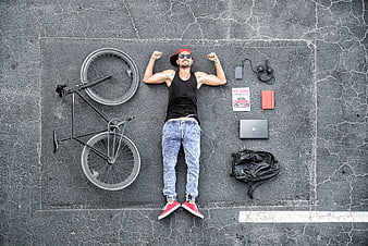 Top view of man lying on asphalt with bicycle and tech essentials