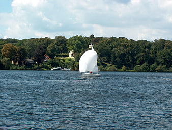 White sailboat gliding on a lake with forested shoreline