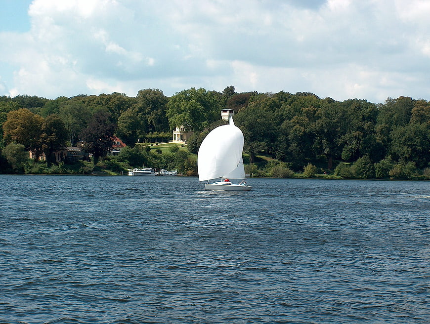 White sailboat gliding on a lake with forested shoreline