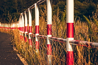 Red and white roadside safety barrier with tall dry grass