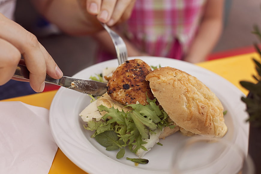 Close-up of hands cutting a grilled chicken sandwich with greens