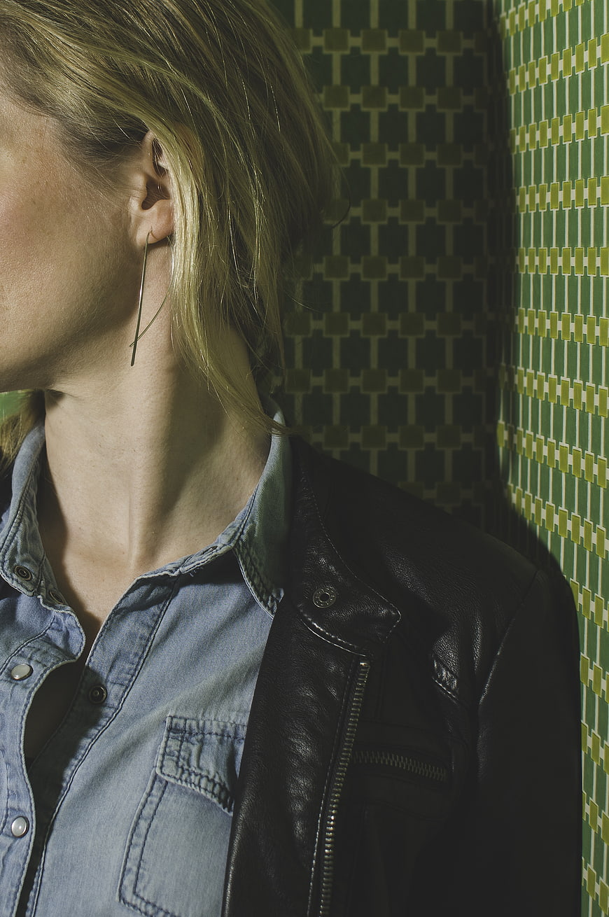 Close-up of woman in denim shirt and leather jacket against green patterned wall