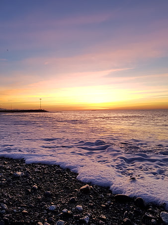 Sunset over pebble beach with foamy waves and distant pier