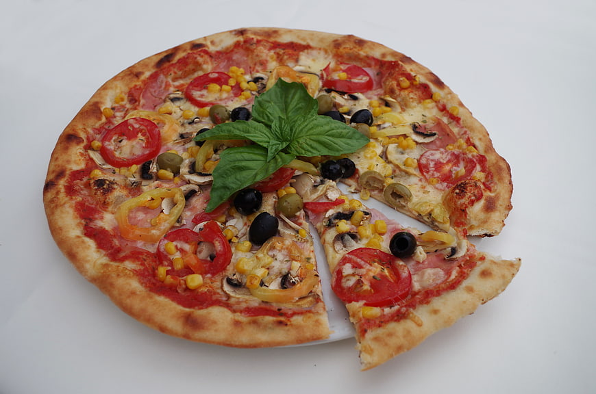 Fresh vegetable pizza with basil, olives, and tomatoes on white background