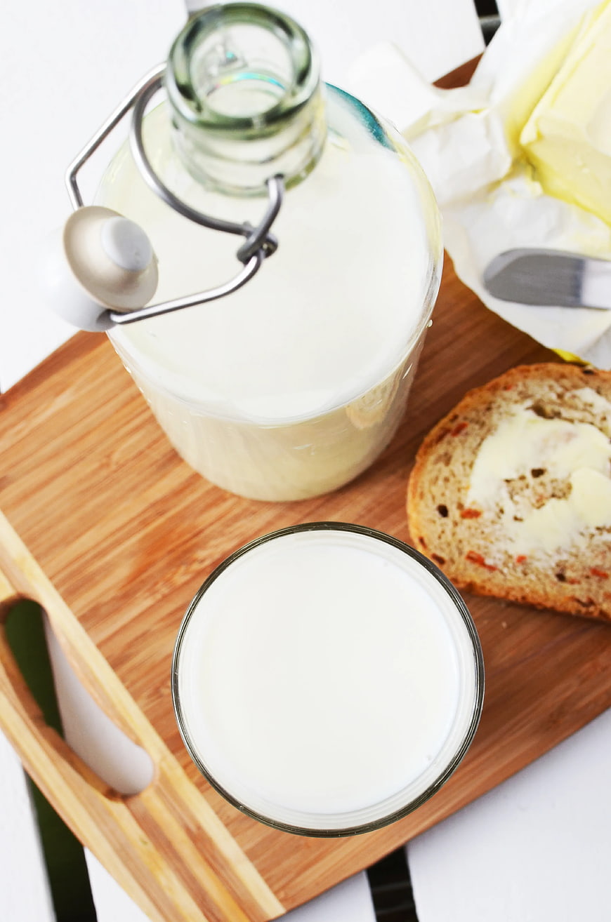 Top view of milk bottle, glass, and buttered bread on wooden tray