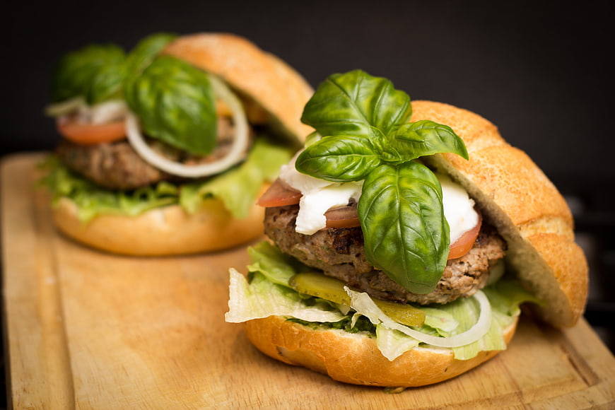 Gourmet burgers with fresh basil on wooden board