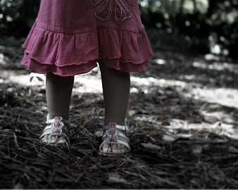 Toddler in pink dress and sandals standing on forest floor