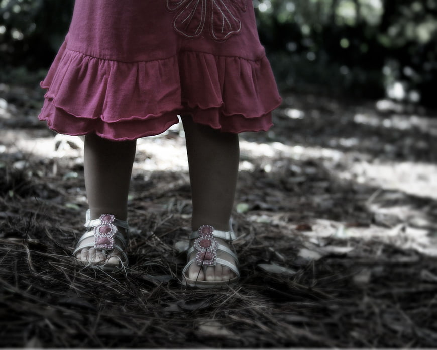 Toddler in pink dress and sandals standing on forest floor