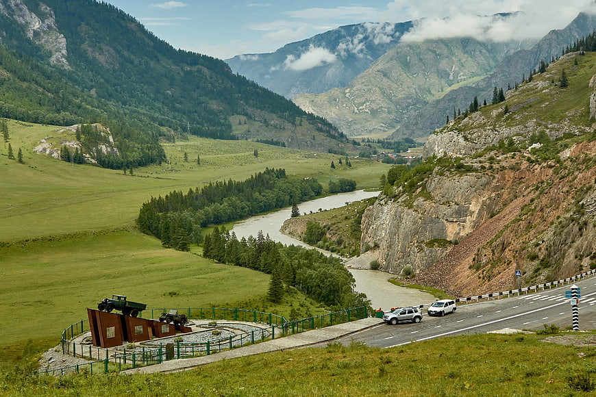 Scenic mountain valley with winding river and roadside memorial