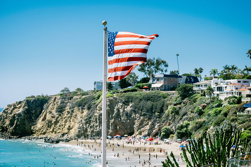 American Flag Waving Over Crowded Beach and Cliffs