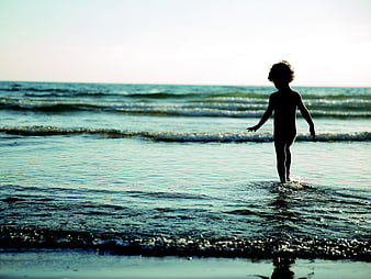 Silhouette of child playing in ocean waves at sunset