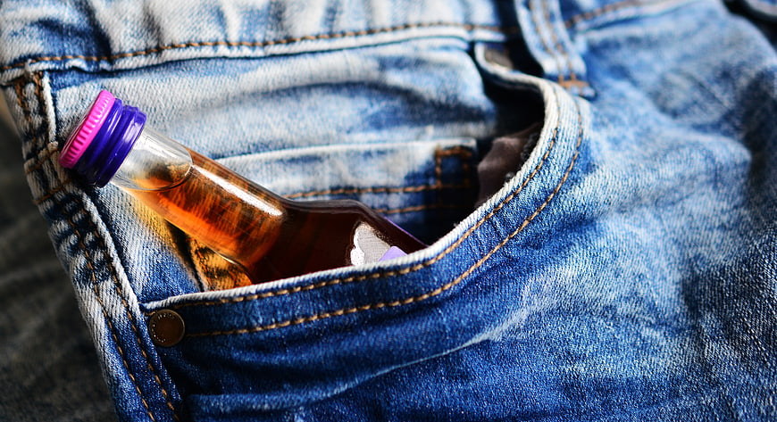 Alcohol bottle tucked into front pocket of blue denim jeans