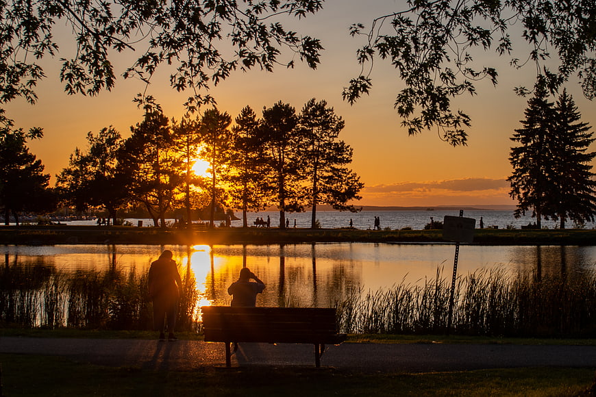 Silhouetted Couple on Park Bench at Sunset by Lake