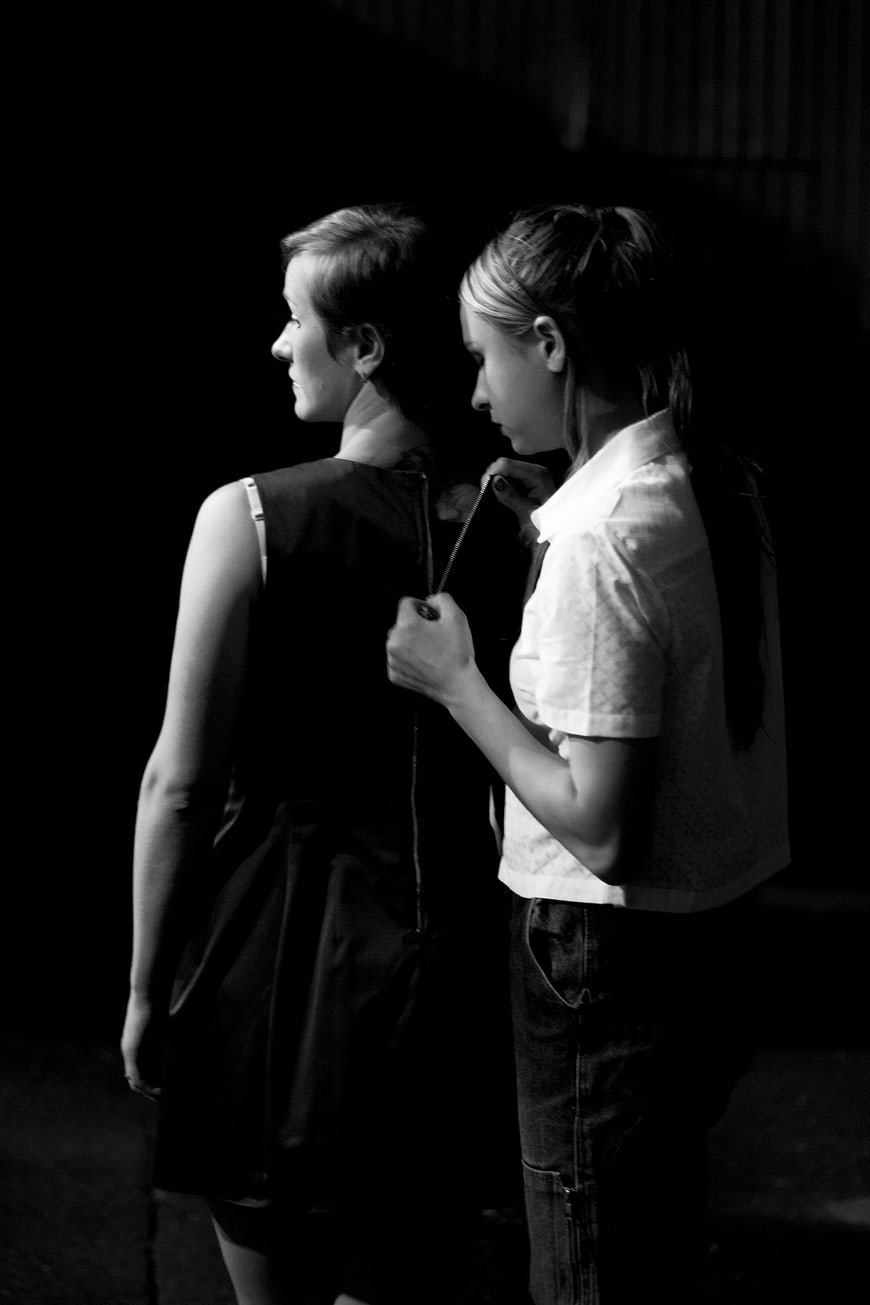 Black and white photo of two women zipping up a dress