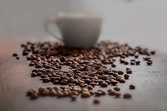 Scattered Coffee Beans on Wooden Table with Blurred Cup