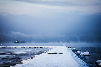 Snowy pier leading into misty blue winter sea