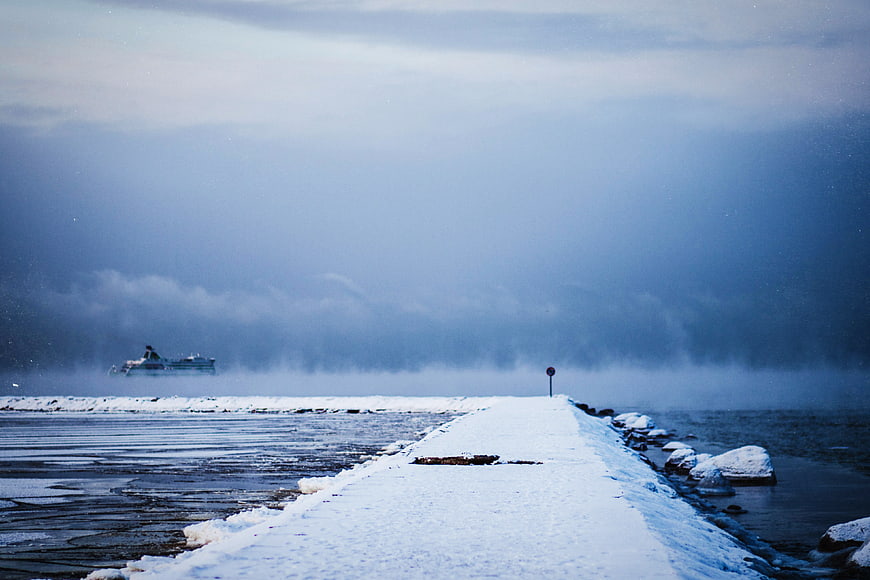 Snowy pier leading into misty blue winter sea
