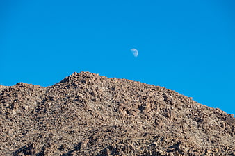Rocky Desert Mountain Peak with Moon in Blue Sky