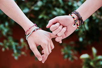 Close-up of two hands holding pinky fingers with bracelets