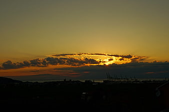 Dramatic sunset over industrial port with cranes and clouds