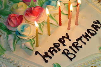 Close-up of a birthday cake with lit candles and piped frosting flowers
