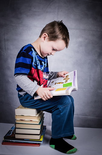 Young boy reading book while sitting on stack of books