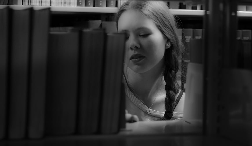 Young woman with braid reading in library black and white