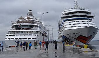 Two large cruise ships docked at a wet pier with passengers