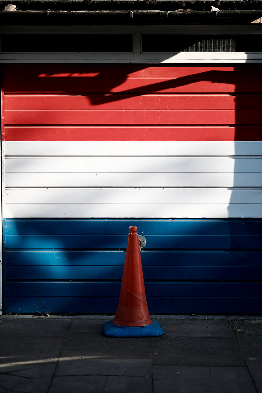 Orange traffic cone against red white blue garage door