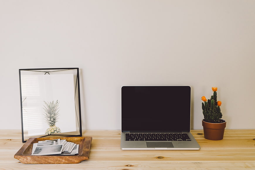 Minimalist workspace with laptop, cactus, and photo tray