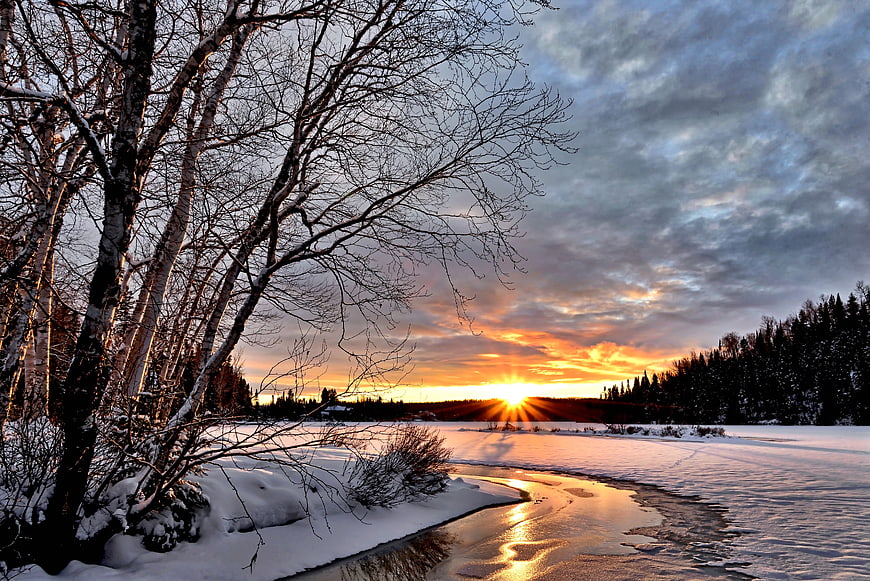 Winter sunset over frozen river with birch trees