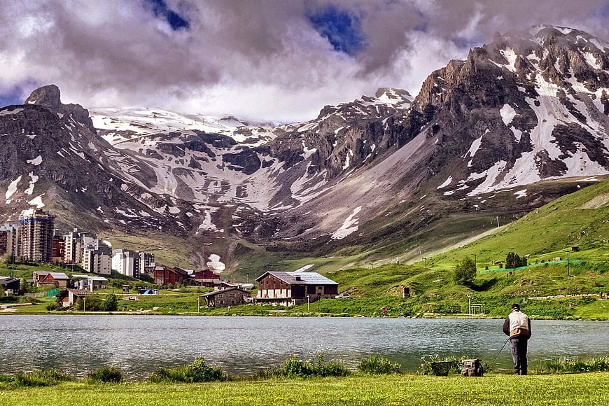 Man Fishing by Lake with Snowy Mountain Resort Background