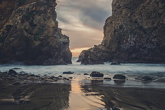 Dramatic Sunset Between Rocky Cliffs on a Misty Beach