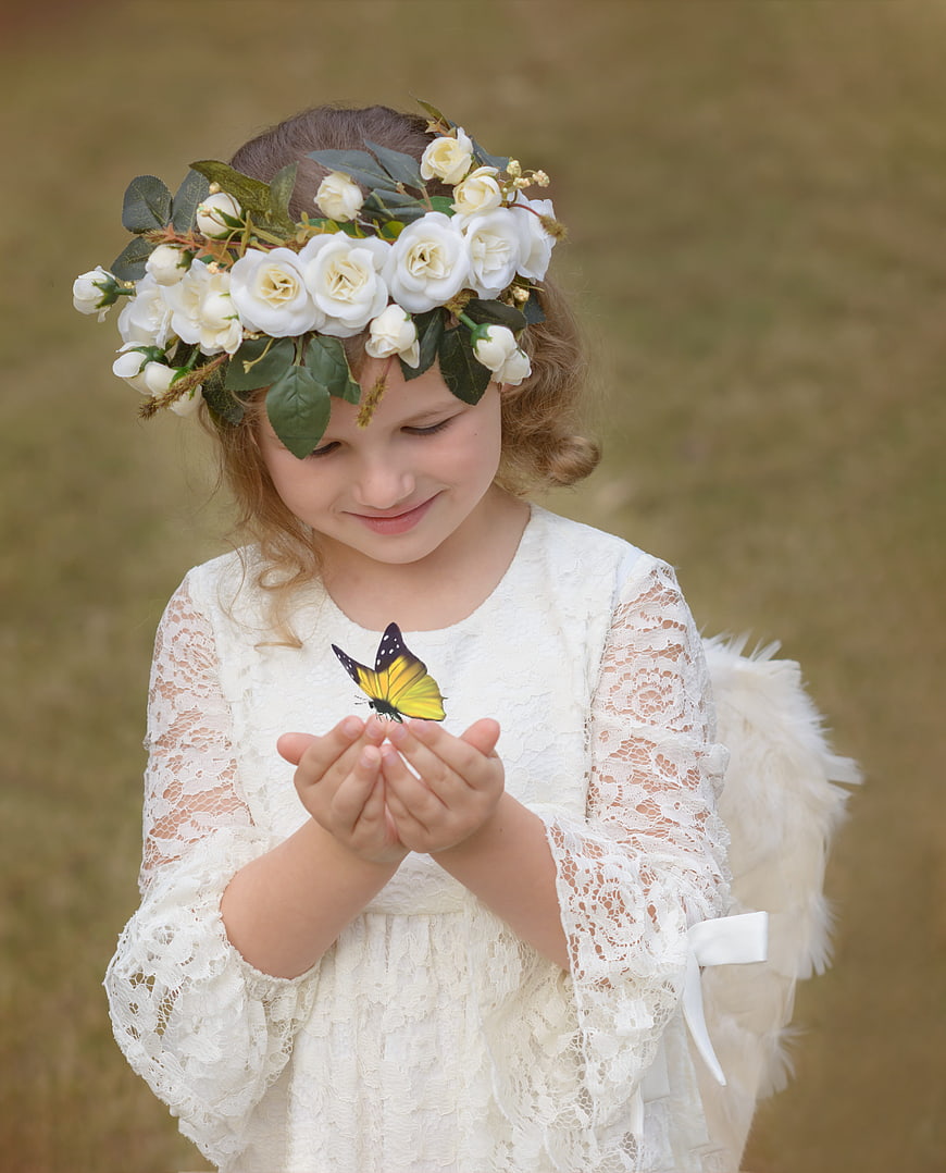 Young girl in white lace dress and flower crown holding a butterfly