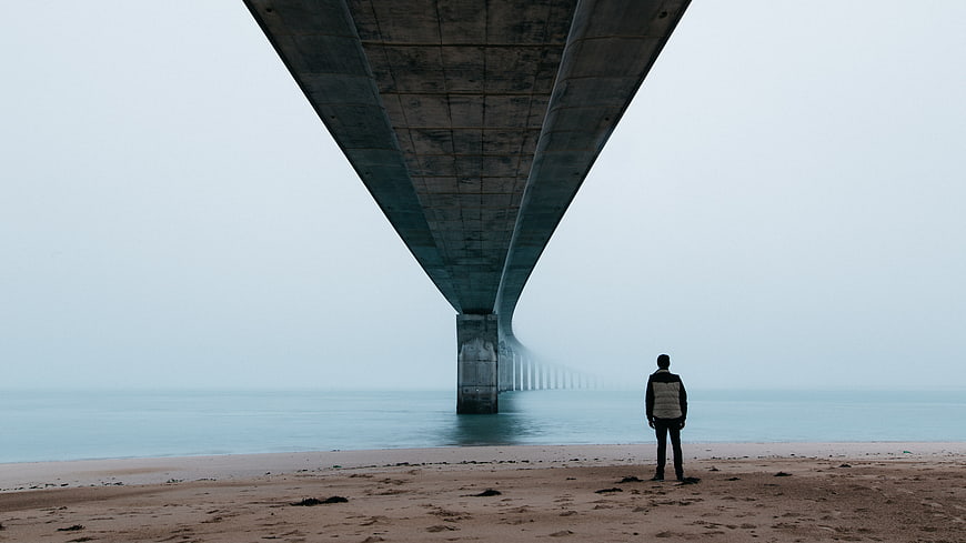 Man standing alone under bridge on foggy beach