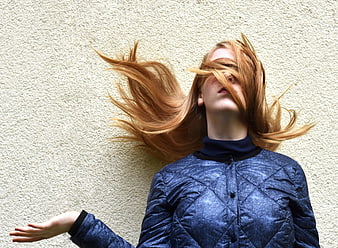 Woman with flying red hair covering face against textured wall